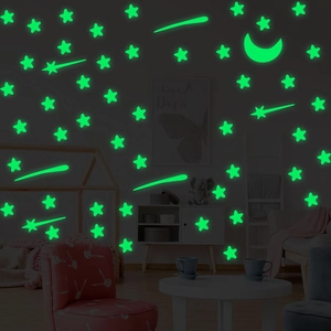 Luminous star and moon wall stickers glowing green in a dark cozy kids bedroom