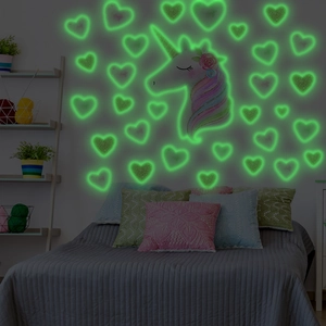 Luminous unicorn and hearts wall stickers glowing green in a dark bedroom setting