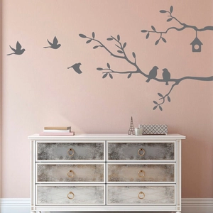 Detail of branch and bird wall sticker above a white dresser in a cozy room