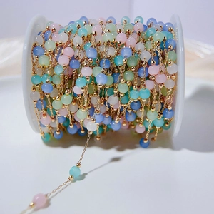 Colorful cat eye stone beads with copper chain on a white spool for DIY jewelry making
