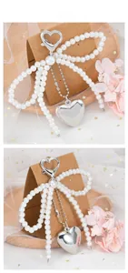 Detail of silver heart charm and bow pendant made of large white pearls with carabiner