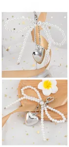 Detail of white pearl bow pendant with silver metallic heart for bags and phones