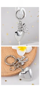 Polished silver heart pendant keychain with bow detail on wooden display tray