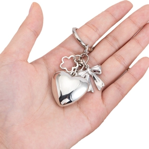 Silver metallic heart keychain with bow and flower charms shown in a hand-held view