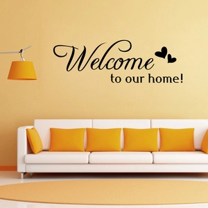 Black 'Welcome to our home!' wall decal with heart accents on warm yellow living room wall