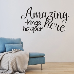 Minimalist 'Amazing things happen here' wall decal above a blue sofa in a modern home