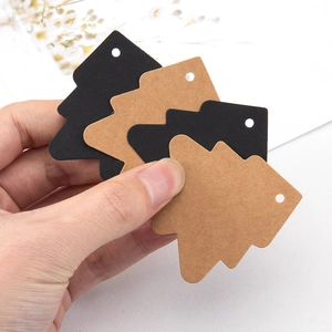 Hand holding Christmas tree shaped kraft paper tags with pre-punched holes for DIY crafts