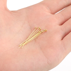 Golden round head pins for jewelry making held in hand to show size and metallic luster