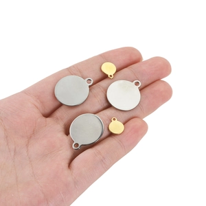 Polished round stainless steel pendants in gold and silver held in palm for size reference