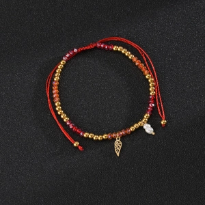 Macro detail of red beaded bohemian bracelet with golden angel wing charm and pearls