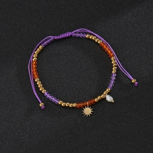 Detail of bohemian purple woven bracelet with gold sun charm and white pearl accent