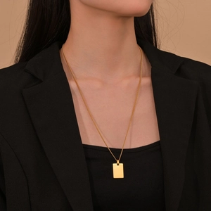 Close-up of a minimalist gold square military tag pendant necklace on a black suit jacket