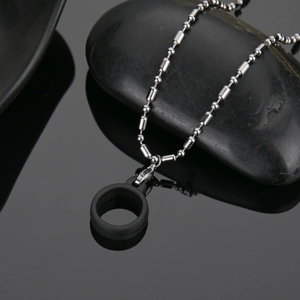 Close-up of black silicone ring with silver stainless steel ball chain on dark pebbles
