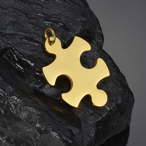 Polished gold puzzle piece pendant in stainless steel displayed on a black natural rock