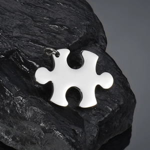 Polished puzzle piece pendant in stainless steel displayed on a black mineral stone base