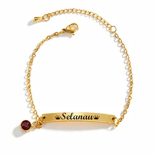 Detalle de pulsera dorada para niños con placa grabada, corona y piedra roja