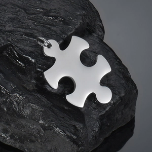 Detailed macro view of a polished stainless steel puzzle piece pendant on dark natural stone