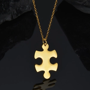 Detailed view of a polished gold puzzle piece pendant on a slim cross chain necklace
