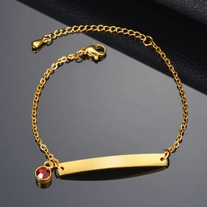 Detalle de la pulsera dorada con placa pulida y dije de cristal rojo de estilo lujoso