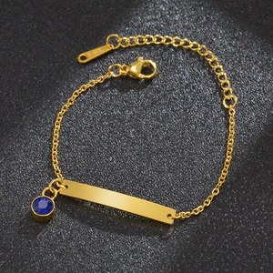 Detalle de una pulsera de acero inoxidable dorado con circón azul sobre fondo negro mate