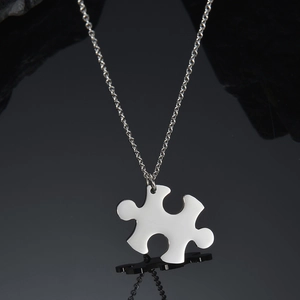 Polished stainless steel puzzle piece pendant with silver chain on black reflective surface