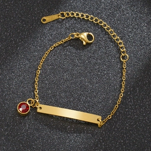Detalle de pulsera de acero dorado con circón rojo y placa para grabado personal