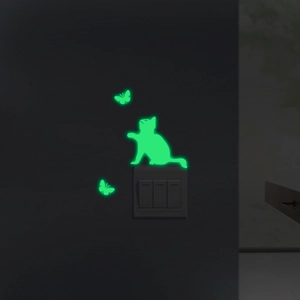 Luminous green silhouette of a cat and butterflies glowing on a dark wall switch