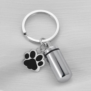 Detailed macro view of paw print charm and cylinder memorial urn keychain on fabric