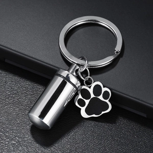 Stainless steel pet memorial cylinder keychain with paw print charm on black leather background