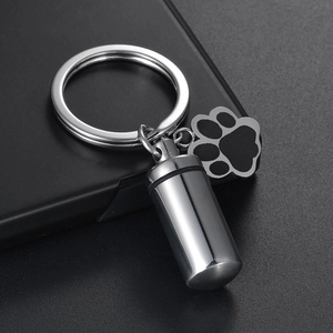 Polished stainless steel cylinder urn keychain with black paw print charm on dark surface