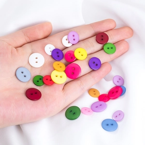 Bottoni colorati in resina per cucito e fai da te tenuti in mano su seta bianca