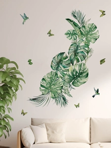Detail of tropical monstera leaves and hummingbirds wall decals above a living room sofa