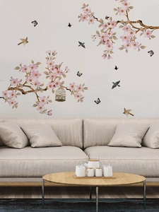 Detail of pink cherry blossom wall decal with birds and cage above a cozy beige sofa