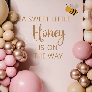Pink bee baby shower backdrop with gold text and decorative balloon arch for parties