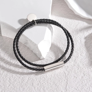 Pulsera de cuero trenzado negro de doble capa con cierre de acero sobre piedra blanca