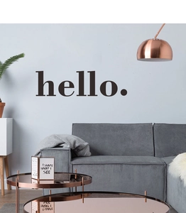 Minimalist 'hello.' wall sticker decal in black serif font above a modern fabric sofa