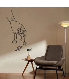 Artistic wall decal featuring minimalist black hand holding planets and stars on a beige wall