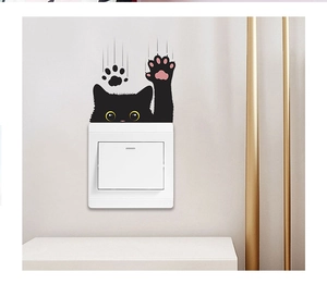 Detail of cute black cat wall sticker with yellow eyes and pink paws over a white light switch