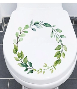 Close-up of a green leaf wreath decal applied on a white toilet lid in a bathroom