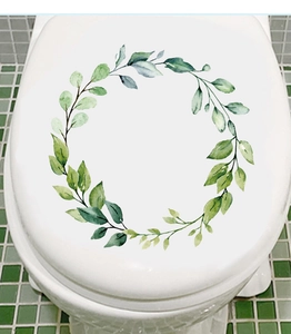 Detail view of green leaf wreath toilet lid decal on white surface with tile background