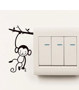 Détail d'un autocollant singe noir suspendu à une branche décorant un interrupteur mural