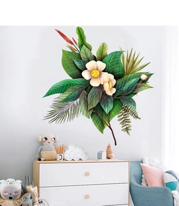 Dettaglio degli adesivi murali con foglie tropicali verdi e fiori bianchi su muro bianco