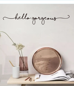 Detail of hello gorgeous black cursive script wall decal on a minimalist white wall background