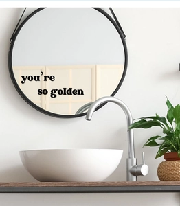 Detail showing 'you’re so golden' black art wall decal sticker on a round bathroom mirror