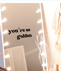 Close-up of black retro You're So Golden mirror decal sticker on a lighted vanity mirror