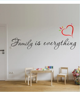 Détail du sticker mural Family is everything avec cœur rouge sur un mur de salon blanc