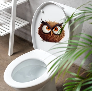 Detail view of a cartoon angry owl sticker on a white toilet lid in a modern bathroom