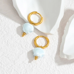 Macro detail of gold-plated hoop earrings featuring light blue shell pendants
