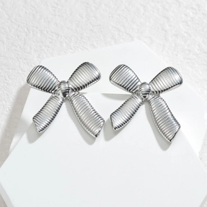 Polished silver stainless steel bow earrings with striped texture on white geometric stand