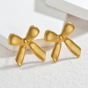 Minimalist gold bow earrings with textured finish on a white geometric display